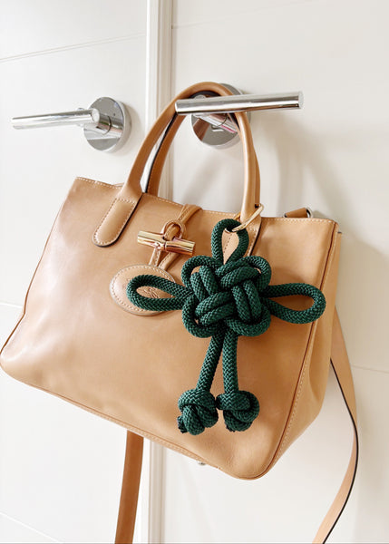 Traditional Chinese fortune knot in a deep emerald green color in a jumbo size, attached to a leather handbag.